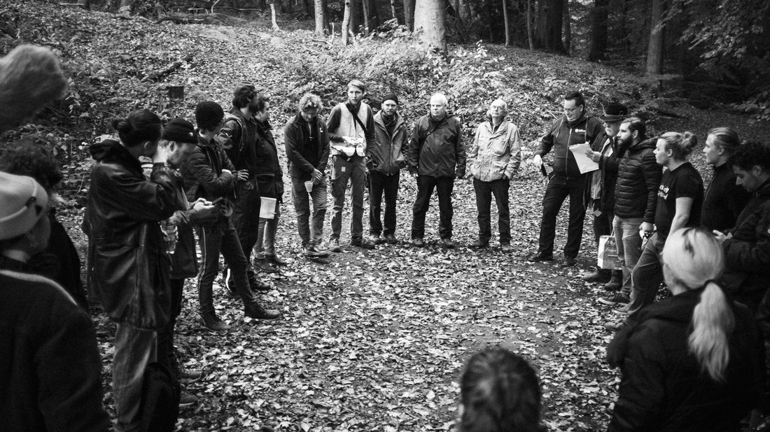 Rund zwei Dutzend Beteiligte stehen im Wald im Kreis, eine Ansprache mit Drehplan in der Hand